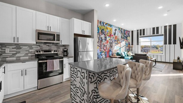 A modern kitchen with white cabinets, stainless steel appliances, a patterned island, and a colorful abstract mural. - Sleek 1BR Near Broadway - Comfort & Convenience! (Nashville)