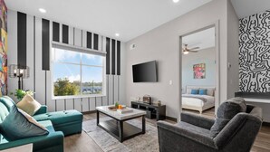 A modern living room with a large window, a flat-screen TV, a sofa, a coffee table, and a patterned rug. - Sleek 1BR Near Broadway - Comfort & Convenience! (Nashville)