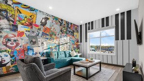A living room with a vibrant mural, a teal sofa, a grey armchair, and a coffee table. - Sleek 1BR Near Broadway - Comfort & Convenience! (Nashville)