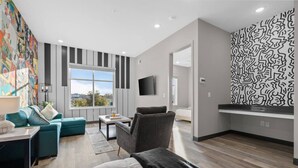 A modern hotel room with a large window, a sofa, a chair, a bed, a TV, and a patterned wall. - Sleek 1BR Near Broadway - Comfort & Convenience! (Nashville)