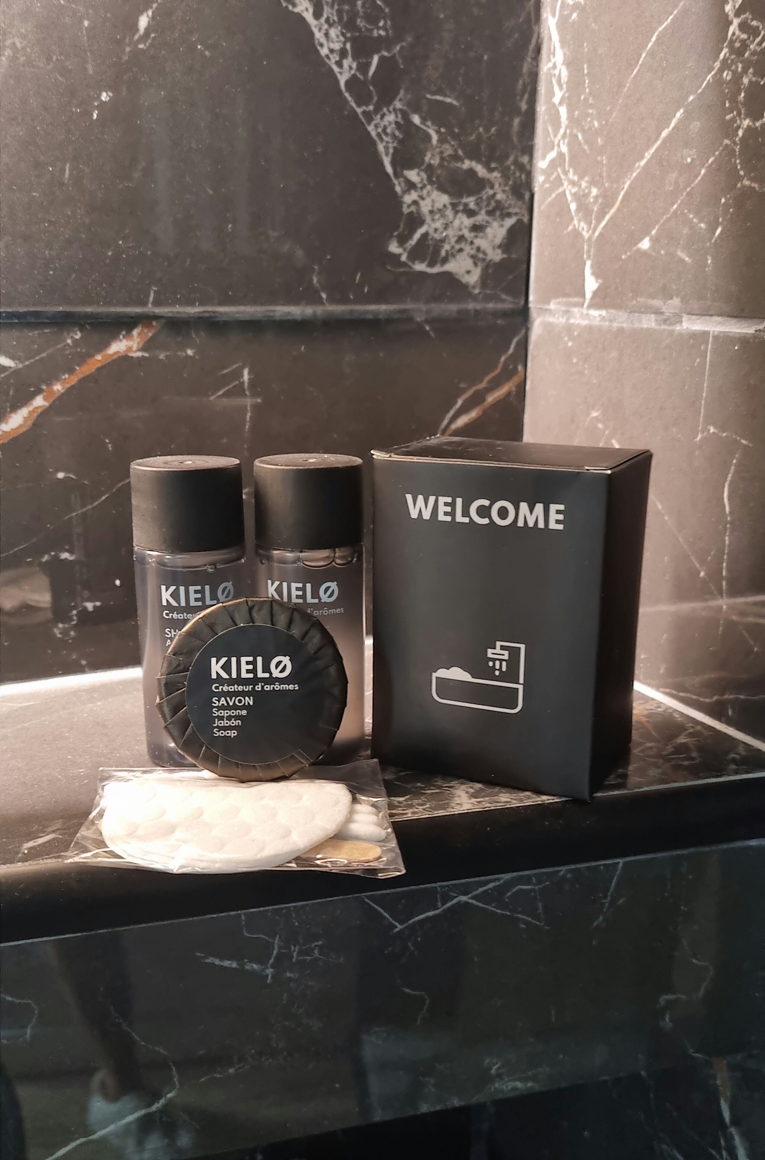 En badrumsmöbel med en svart marmorskiva, två flaskor tvål från Kiehl's, en tvålkopp och en svart låda med texten "VÄLKOMMEN".