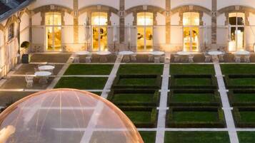 Un grand hôtel à la façade symétrique, doté d’une cour intérieure où l’herbe est soigneusement entretenue, ainsi que d’espaces extérieurs aménagés pour se détendre.