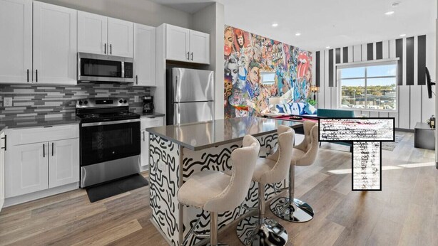 A modern kitchen with white cabinets, stainless steel appliances, a colorful mural, and a bar area with a patterned countertop and bar stools.