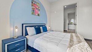 A bedroom with a bed, nightstands, a wall art piece, and a door leading to a bathroom.