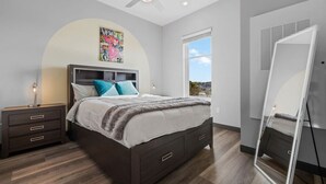 A bedroom with a bed, bedside tables, a ceiling fan, a large window, and a mirror.