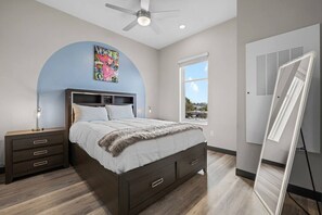 Une chambre à coucher comprenant un lit, une table de chevet, un ventilateur de plafond, une fenêtre et un tableau blanc.