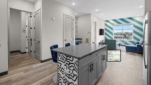 Een moderne keuken met een centraal eiland, een eetgedeelte met blauwe stoelen, en een woonkamer met een groot raam.