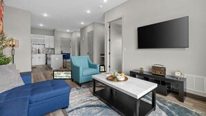 Een moderne woonkamer met een bank, een salontafel, een televisie en een keuken op de achtergrond.