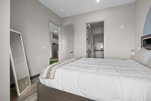 A bedroom with a large bed, a wardrobe, and a mirror. There is a door leading to a bathroom and a hallway.