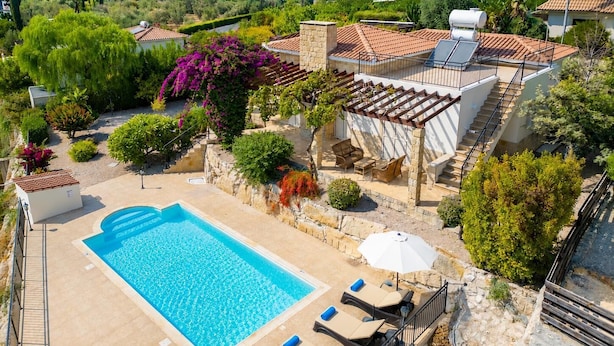 Zona de piscina con vista despejada al mar, un área de estar al aire libre cubierta y una pared de piedra.