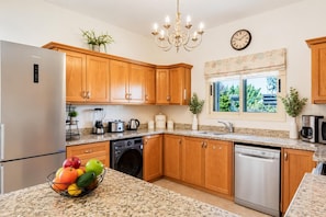 A kitchen with wooden cabinets, granite countertops, a stainless steel refrigerator, a dishwasher, a washing machine, and a coffee maker.