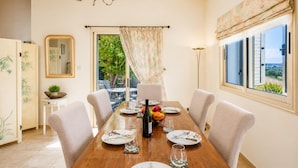 Comedor con mesa de madera, sillas, candelabro, espejo y vistas al exterior con vegetación.