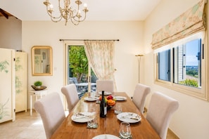 A dining room with a wooden table, chairs, a chandelier, a mirror, and a view of greenery outside.