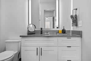 A bathroom with a toilet, a sink with a mirror, and a towel rack. - 1BR Music Retreat near Honky-Tonks & Broadway! (Nashville)