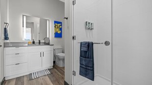 Un baño moderno con muebles blancos, ducha y toallero.