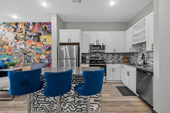 A modern kitchen with white cabinets, stainless steel appliances, and a colorful mural on the wall.