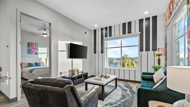 Ein modernes Wohnzimmer mit einer Couch, einem Couchtisch, einem Fernseher und einem großen Fenster mit Blick auf die Stadt.