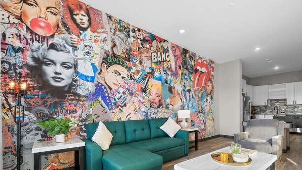 A living room with a green sectional sofa, a coffee table, and a vibrant graffiti wall.