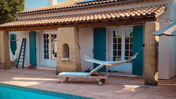 Un espace aménagé au bord de la piscine, comprenant un hamac, une chaise longue et une piscine carrelée avec un bord décoratif.