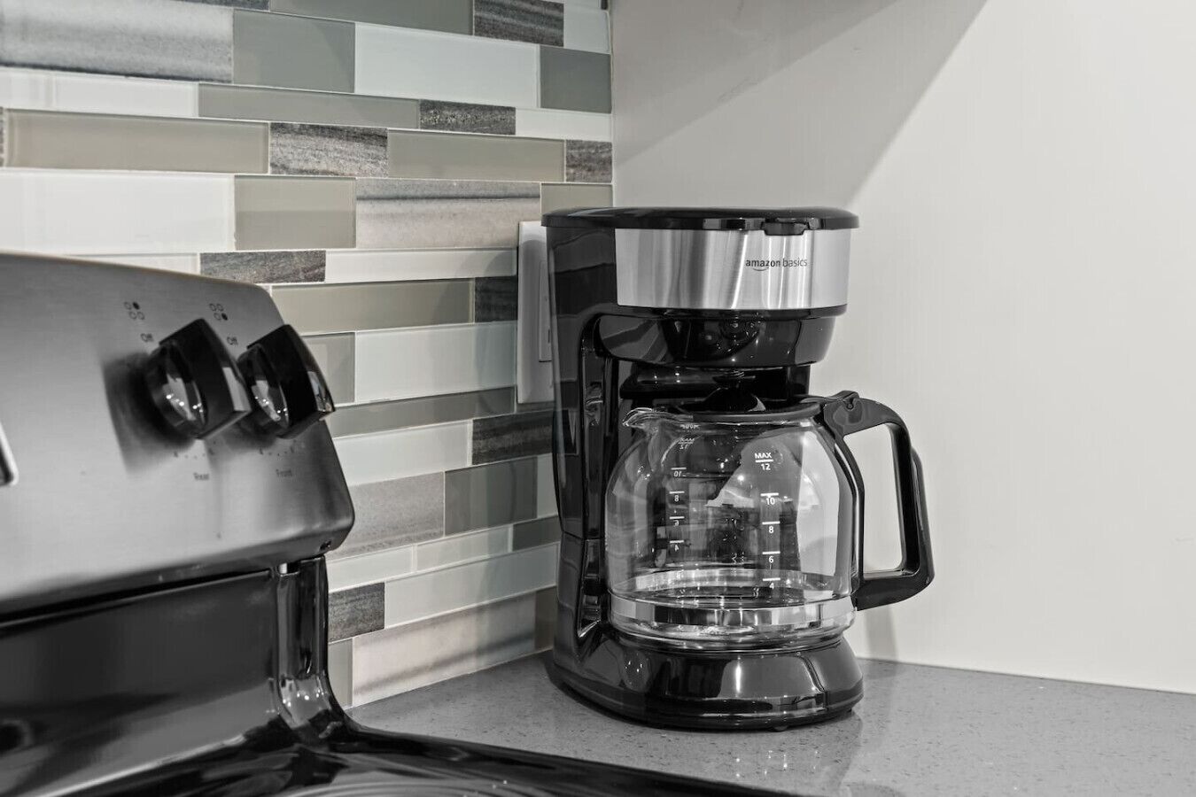 A coffee maker with a clear glass carafe and a black base, positioned on a kitchen counter with a tiled backsplash.