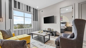 A modern living room with a sofa, armchair, coffee table, and a flat-screen TV mounted on the wall. - 1BR Haven – Quick Drive to Honky Tonks & More! (Nashville)