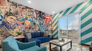 A living room with a vibrant mural, a blue sofa, a coffee table, and a view through a sliding glass door. - Cozy 1BR Escape – Close to the Heart of Nashville! (Nashville)