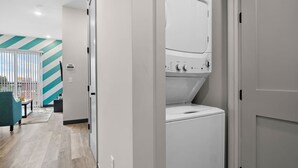 A laundry room with a front-loading washer and dryer, a teal-striped wall, and a view of the outside through a window. - Cozy 1BR Escape – Close to the Heart of Nashville! (Nashville)
