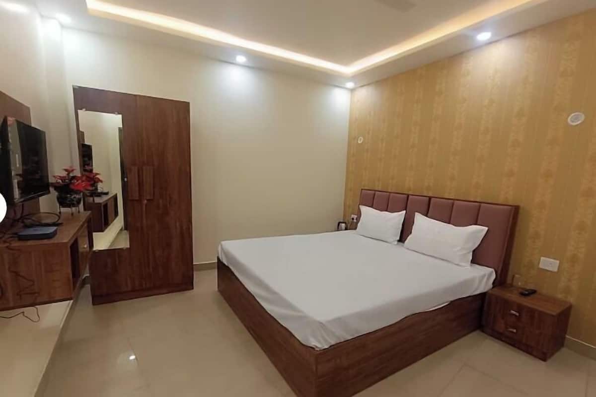 A bedroom with a bed, wooden headboard, bedside tables, a TV, and a mirror.