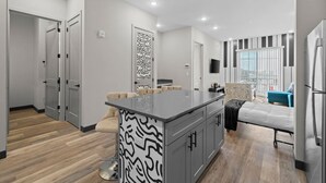 Une cuisine moderne avec un îlot central, un coin repas avec un canapé et une chambre à coucher avec un lit et une fenêtre.