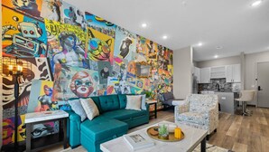 Un salon moderne avec un canapé de couleur turquoise, une table basse et une fresque murale aux couleurs vives.