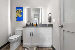 Une salle de bain moderne avec des toilettes blanches, un meuble-lavabo avec un miroir et une œuvre d’art bleue accrochée au mur.