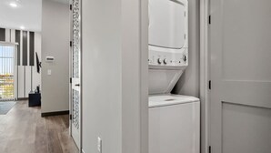 Un cuarto de lavandería con lavadora y secadora de carga frontal, una puerta con panel decorativo y vista al exterior a través de un vidrio.