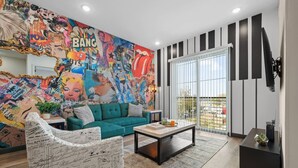 Una sala de estar moderna con un sofá verde azulado, una mesa de centro y un mural colorido en la pared.
