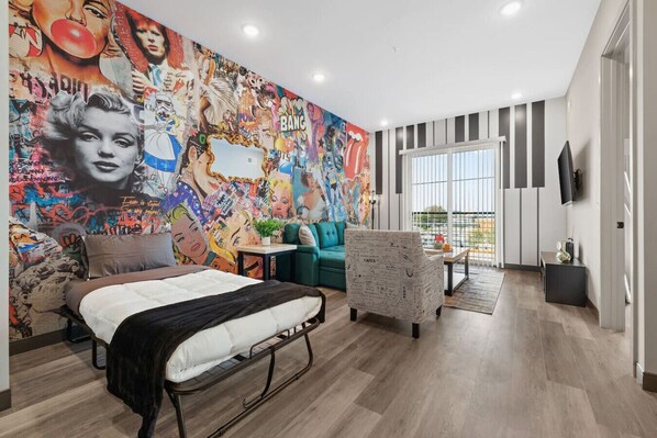 Une chambre moderne avec une grande fresque murale, un lit, un canapé et un téléviseur.
