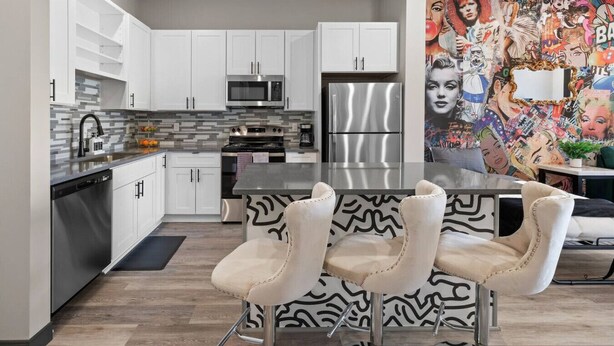 Una cocina moderna con armarios blancos, electrodomésticos de acero inoxidable y un mural colorido en la pared.