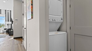 A modern laundry room with a front-loading washer and dryer, a gray wall with a colorful artwork, and a wooden floor.