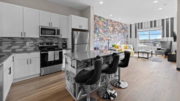 A modern kitchen with white cabinets, a stainless steel refrigerator, and a black countertop with newspaper stools.