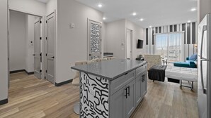 A modern kitchen with a central island, a dining area with a sofa, and a living area with a TV and window.