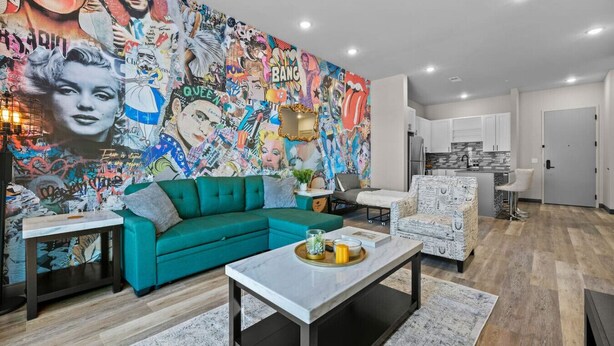 A modern living room with a vibrant mural, a teal sofa, a white armchair, and a marble coffee table.