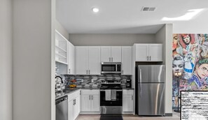 A modern kitchen with white cabinets, a stainless steel refrigerator, a microwave, and a tiled backsplash.