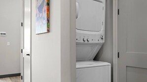 A laundry room with a front-loading washer and dryer, a door, and a wall-mounted light switch.