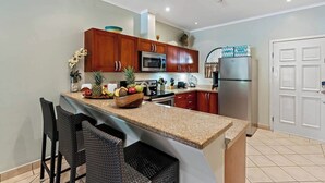 A modern kitchen with wooden cabinets, stainless steel appliances, and a granite countertop. - Sunrise Poolside Oasis Condo – 2BR Tamarindo (Tamarindo)
