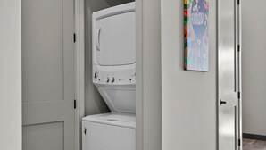 A laundry room with a stacked washer and dryer, a door with a handle, and a wall-mounted colorful artwork.