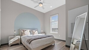 A bedroom with a bed, nightstands, a ceiling fan, a window with blinds, and a mirror with lights. - Urban Oasis 1BR - Quick Access to Downtown Nash! (Nashville)