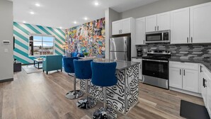 A modern kitchen with white cabinets, stainless steel appliances, and a colorful mural on the wall.
