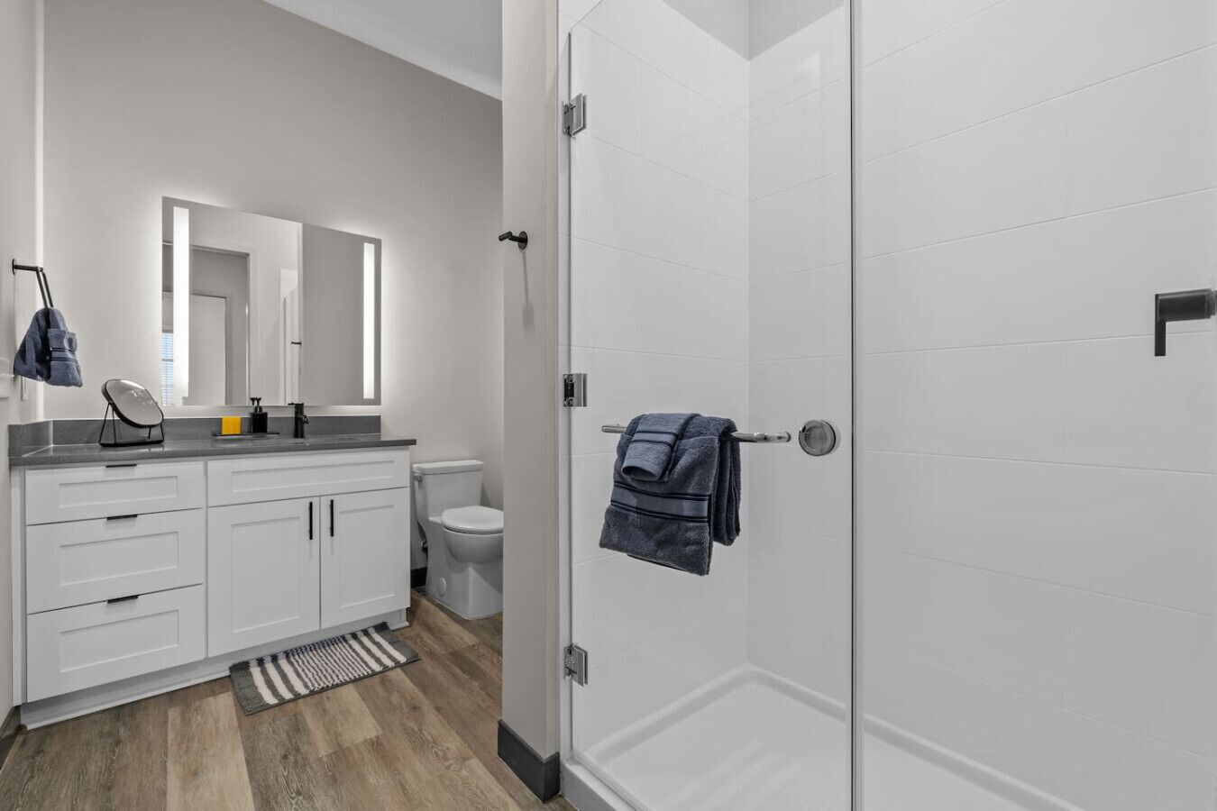 Un baño moderno con muebles blancos, un inodoro, una ducha con puerta de vidrio y una toalla colgada en la puerta.