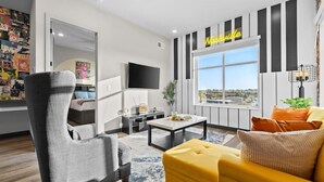 A modern living room with a large window, a flat-screen TV, and a 'Nashville' sign on the wall. - Trendy Oasis: 8 Min to Broadway, Sleeps 4! (Nashville)
