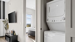Ein moderner Waschraum mit einer Waschmaschine und einem Wäschetrockner mit Frontlader, einem an der Wand montierten Flachbildfernseher und Holzboden.