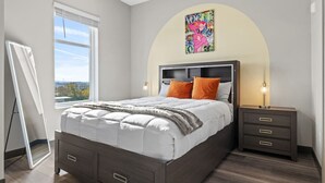 Ein Schlafzimmer mit Bett, Nachttischen, Deckenventilator, Fenster mit Jalousien und Wandbild.