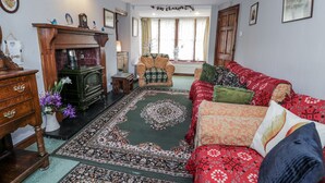 A traditional living room with a patterned rug, a wooden fireplace, and a sofa with patterned cushions. - Old Post Office (Blaenau Ffestiniog)